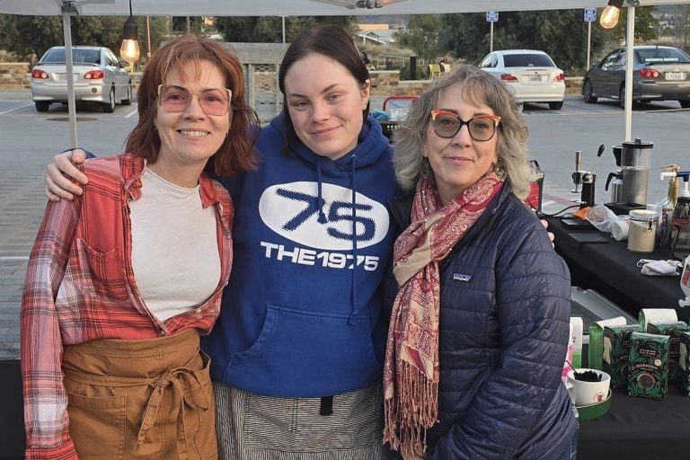 Three women in front of a coffee cart.