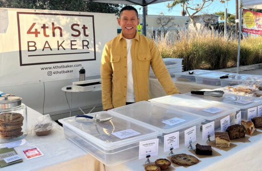 Owner and baker Julien stands smiling with a row of assorted pastries.