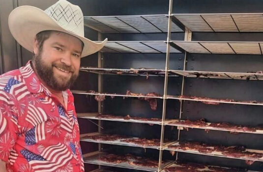 Owner, Big Curt stands in front of racks of beef jerky.