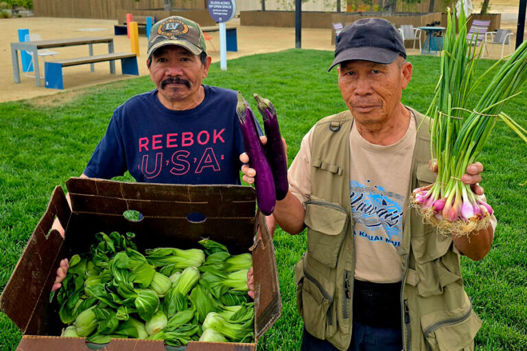 Two men stand with produce.